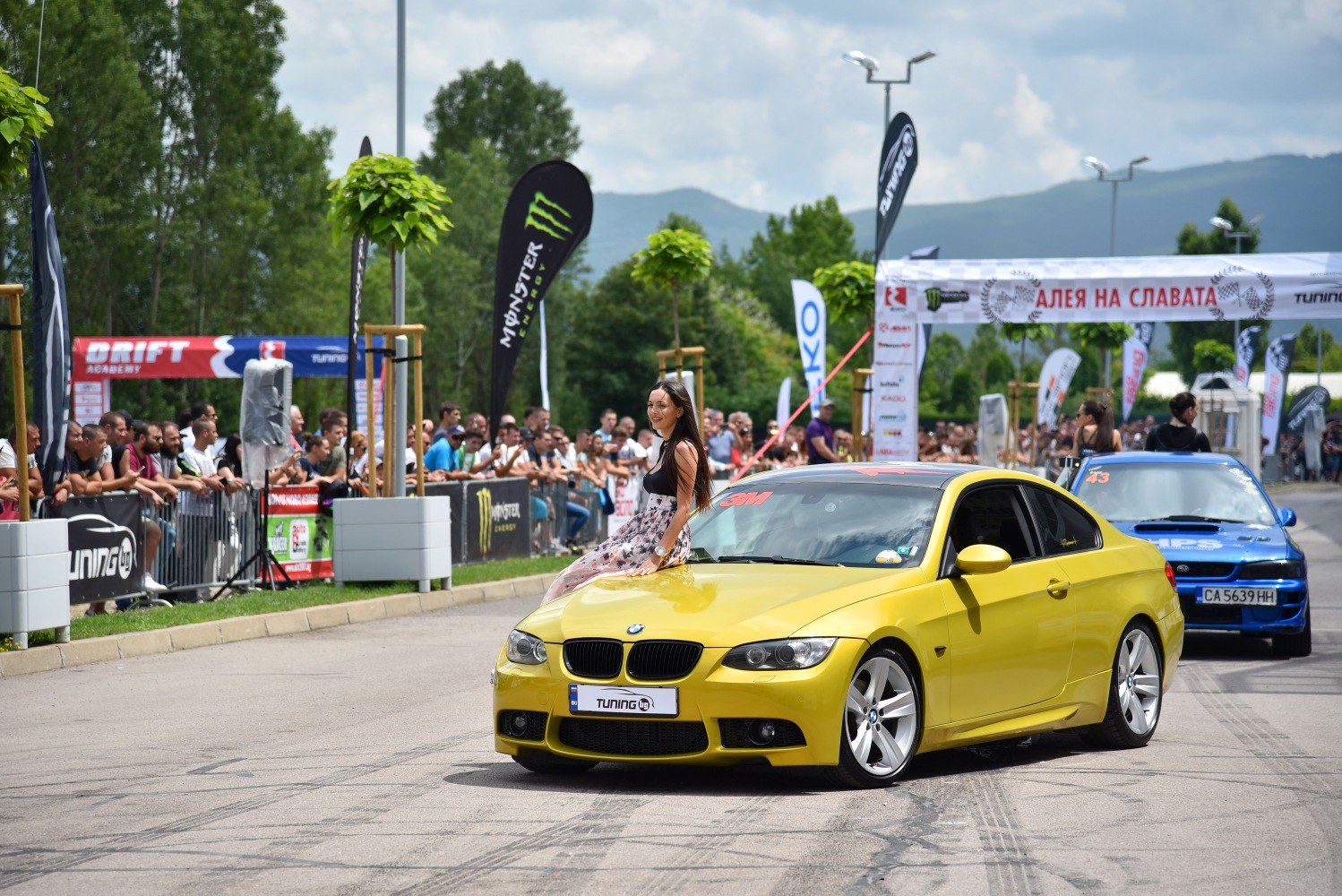 Yellow sports coupe with crowd and drifting event backdrop