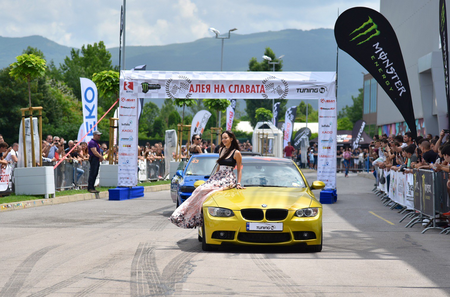 Yellow BMW M3 Coupe front view at event with crowd and banners