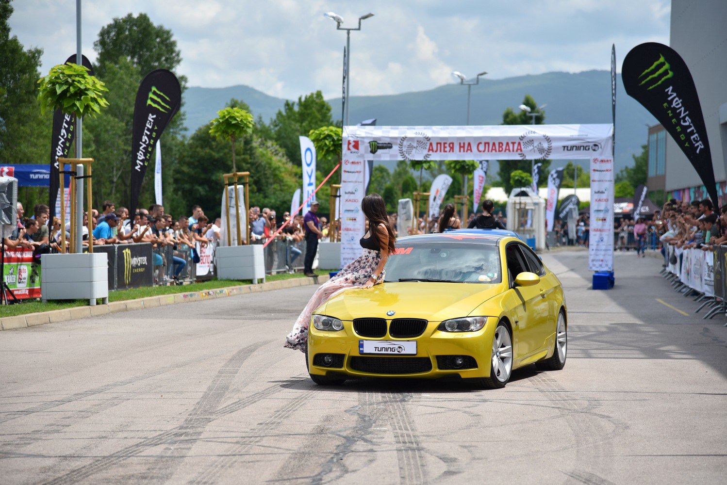 Yellow BMW E92 coupe at a racing event with spectators and banners