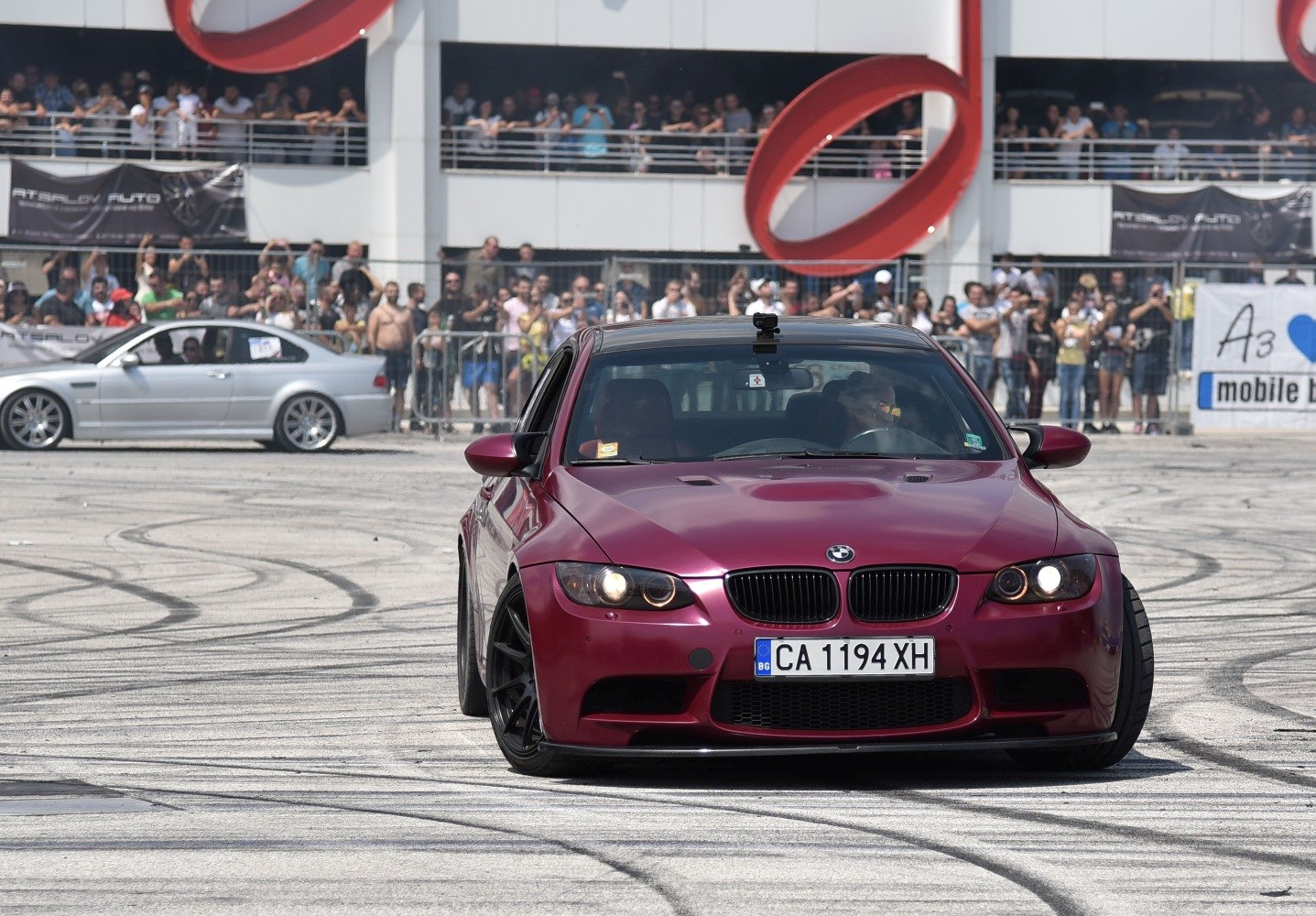 Front view of a red sports coupe with aggressive stance and black wheels at a motorsport event