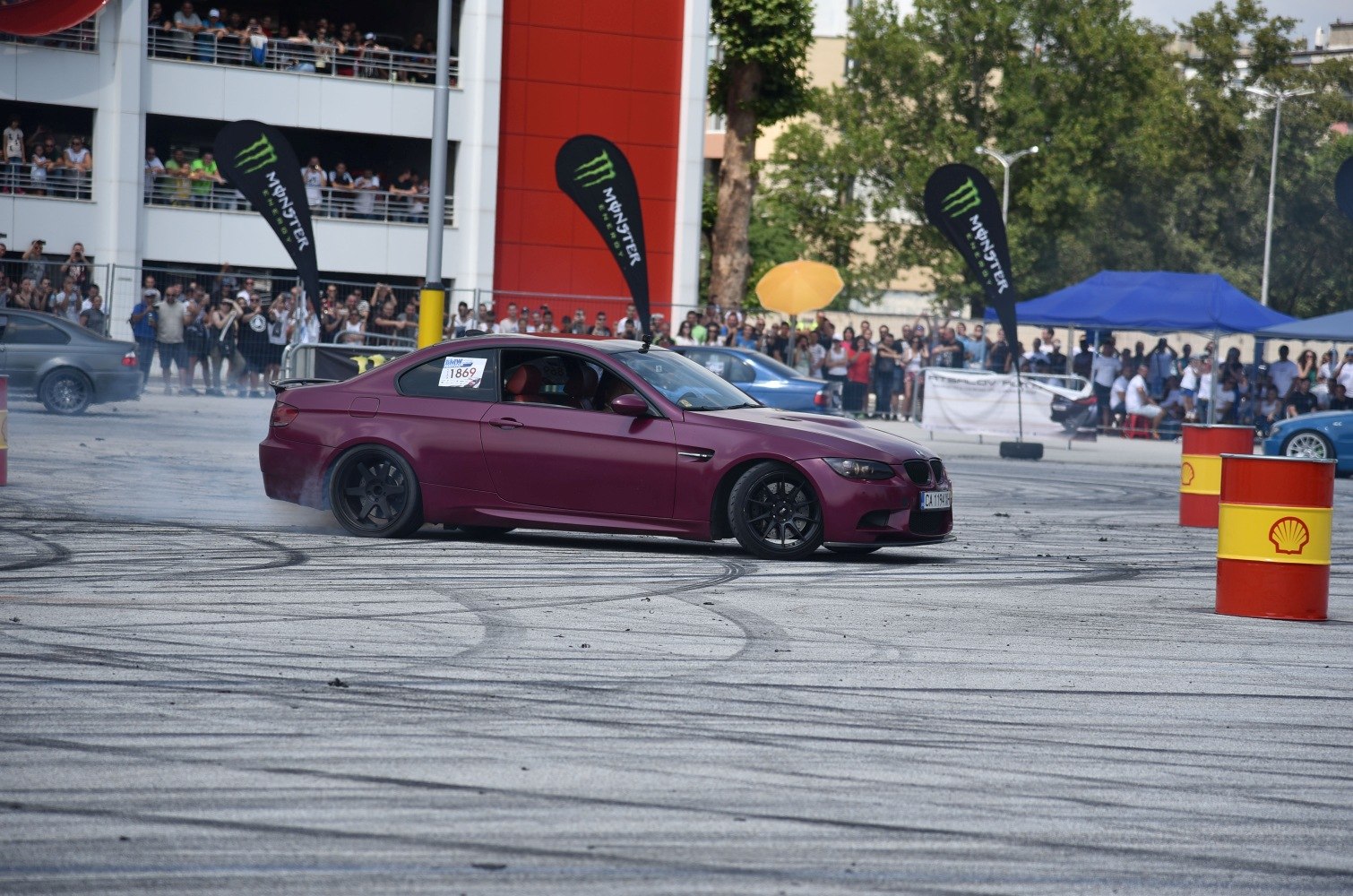 Red coupe drifting on tarmac with tire smoke and crowd in background