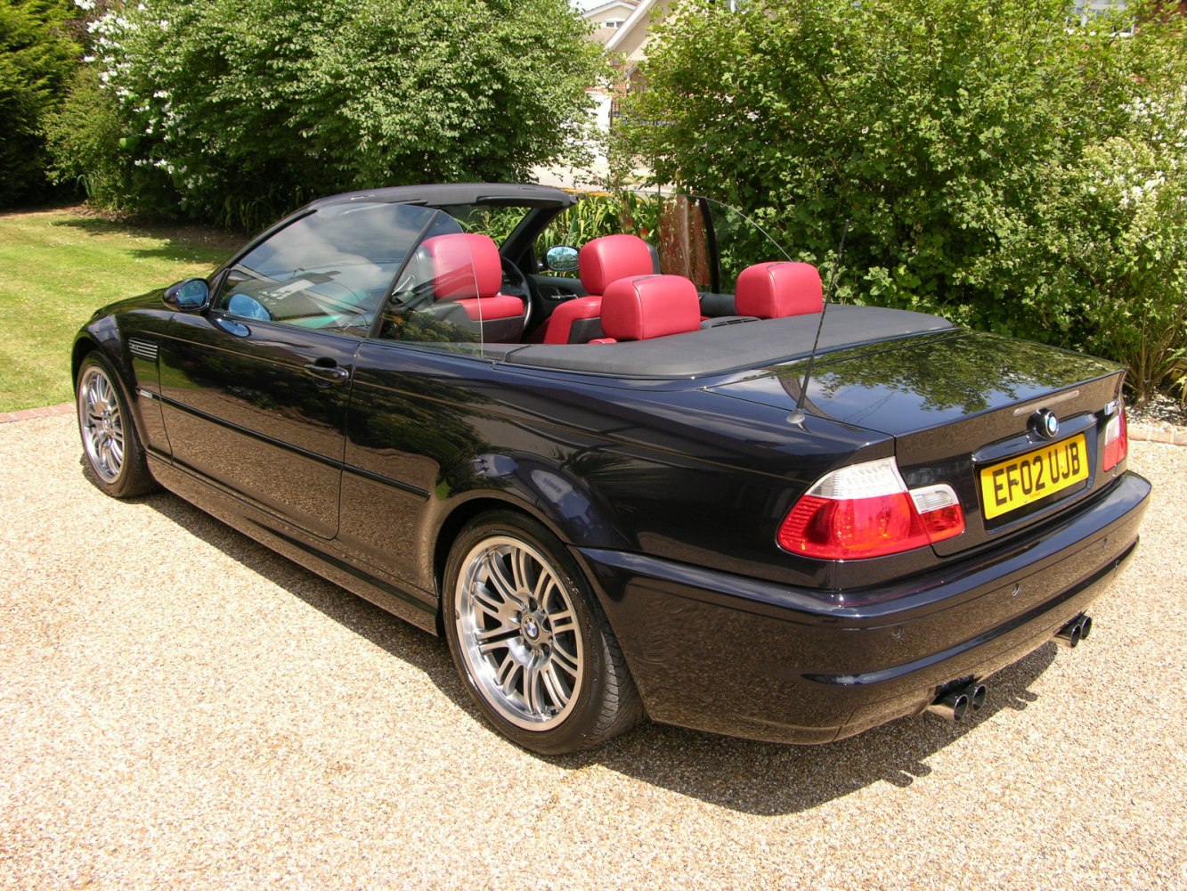 Rear-side view of black convertible with red leather interior and alloy wheels.