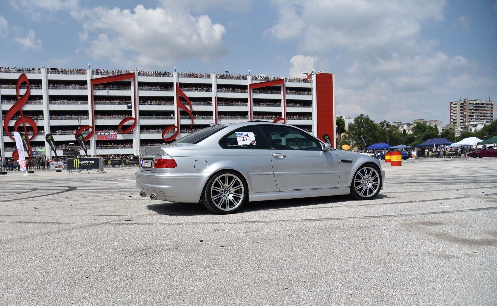 Silver sports coupe side view with multi-floor crowd backdrop