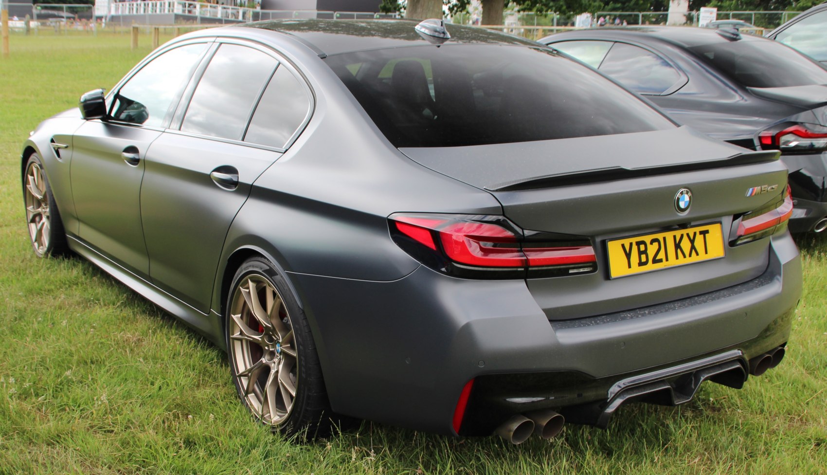 Rear view of a matte-finished sedan with quad exhausts and bronze multi-spoke wheels