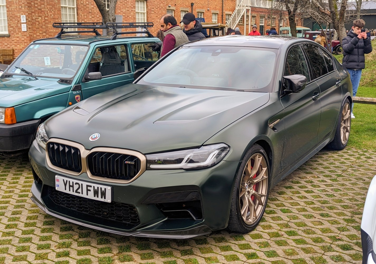 Matte green sedan with bronze multi-spoke wheels and aggressive front grille