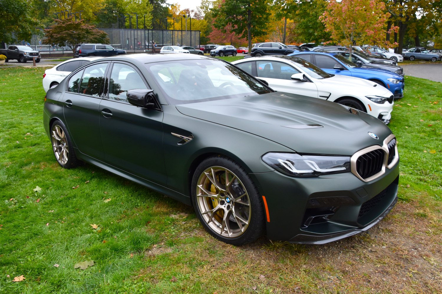 Front side view of matte dark green BMW M5 with gold alloy wheels
