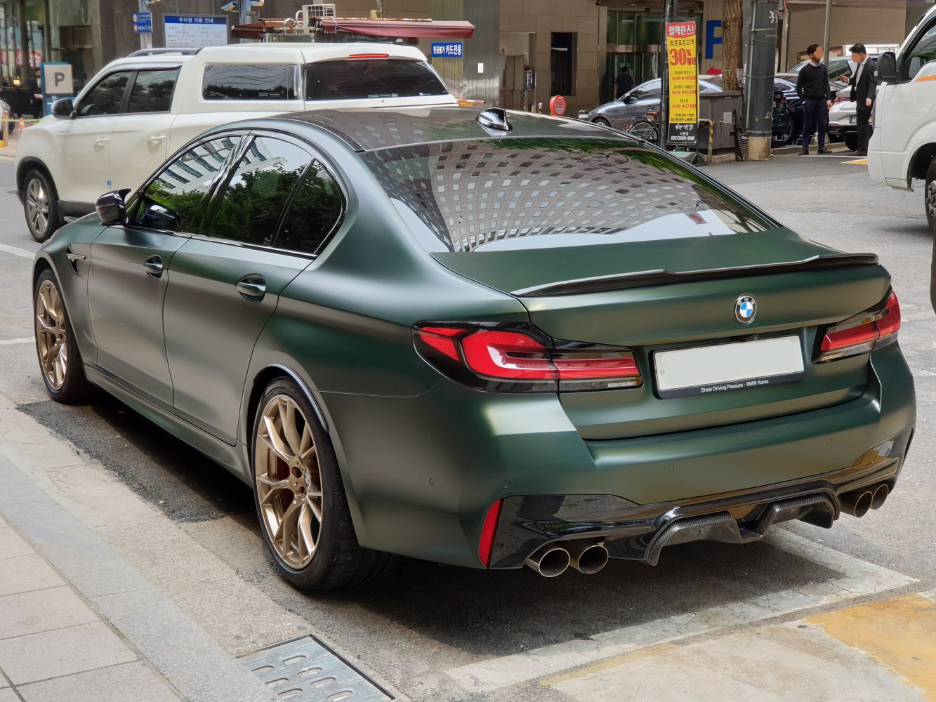 Rear of sporty sedan with quad exhaust tips and matte green paint