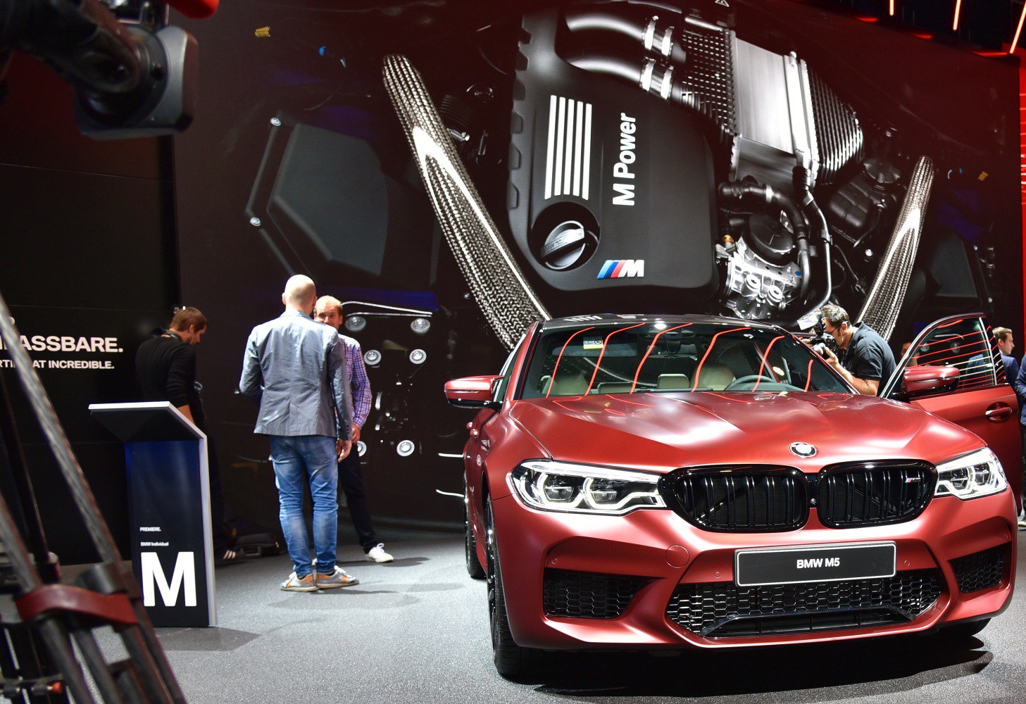 Front view of red BMW M5 F90 with black kidney grille and large M Power engine backdrop