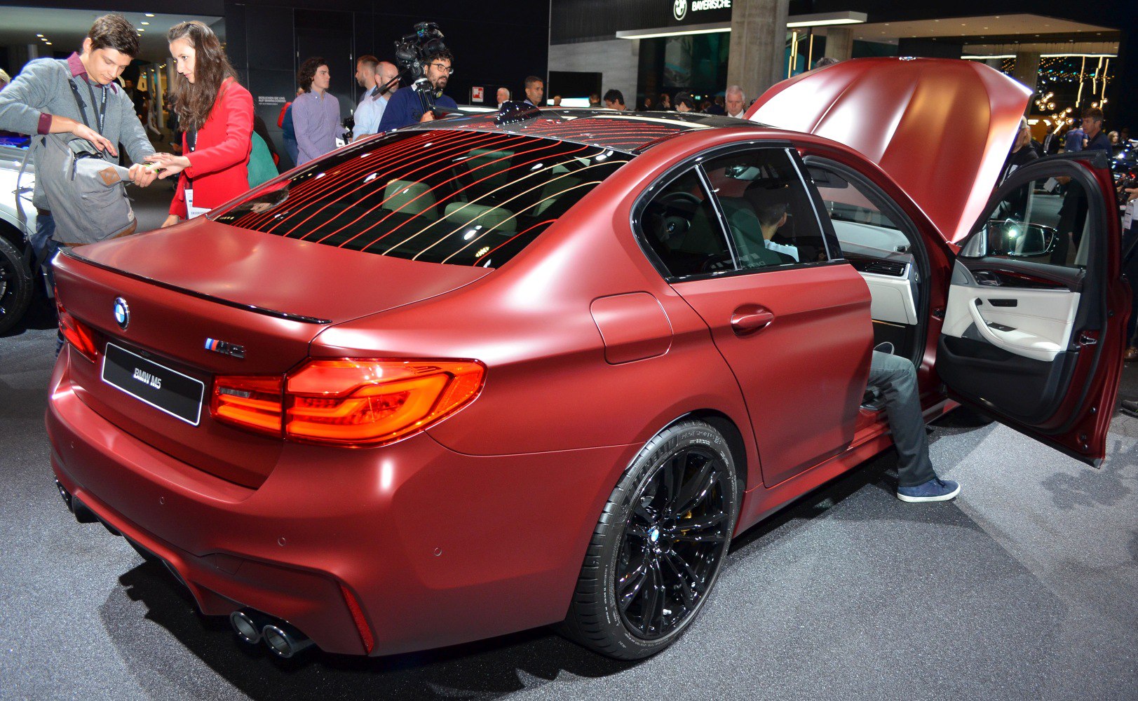 Rear and side view of a sedan with open door and hood, black rims, and quad exhaust pipes