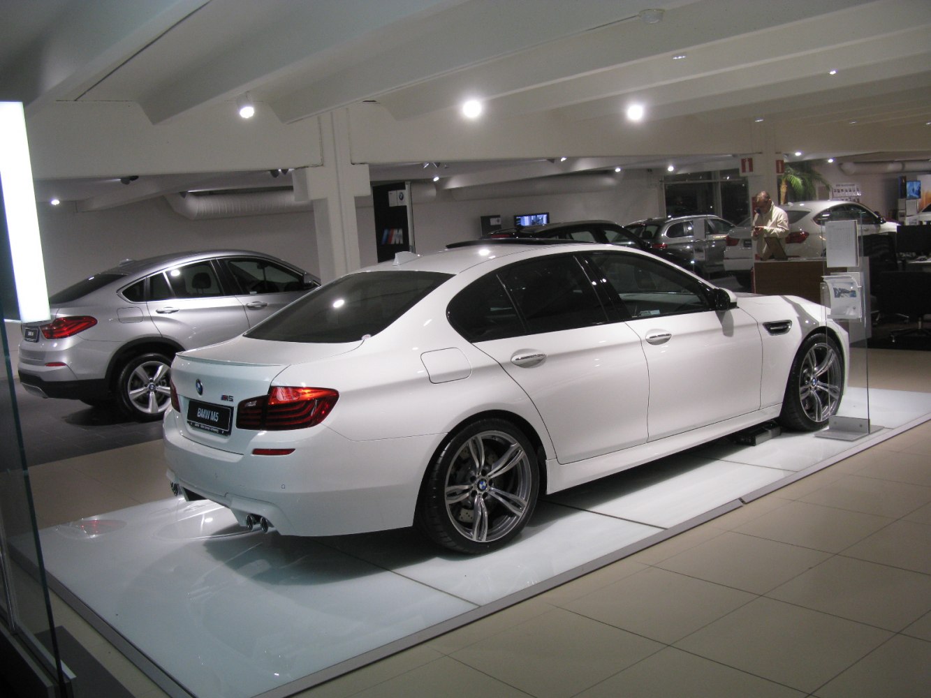 White luxury sedan rear with sporty wheels and dual exhausts under showroom lights