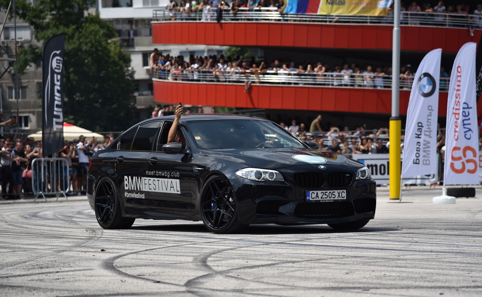 Dynamic black performance sedan with racing rims and crowd