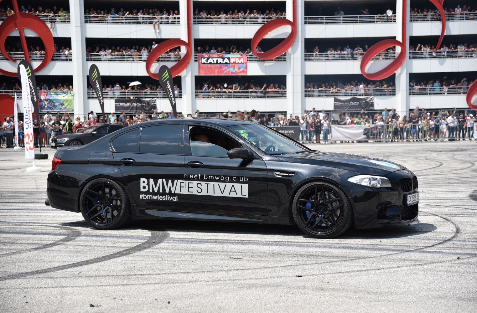 Black sedan with tinted windows and custom black wheels at an outdoor event