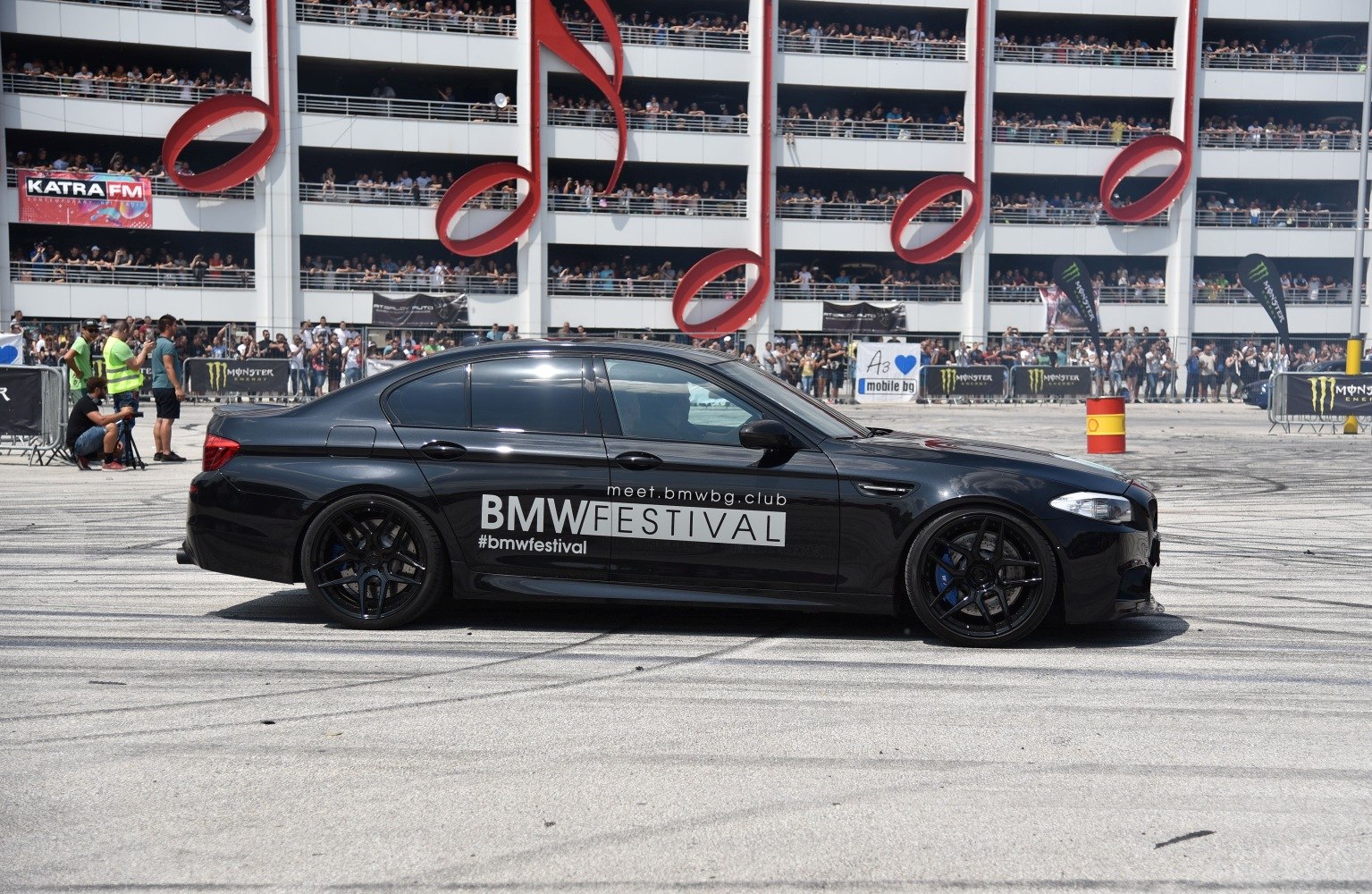Black sedan with sport wheels and blue brake calipers at a festival