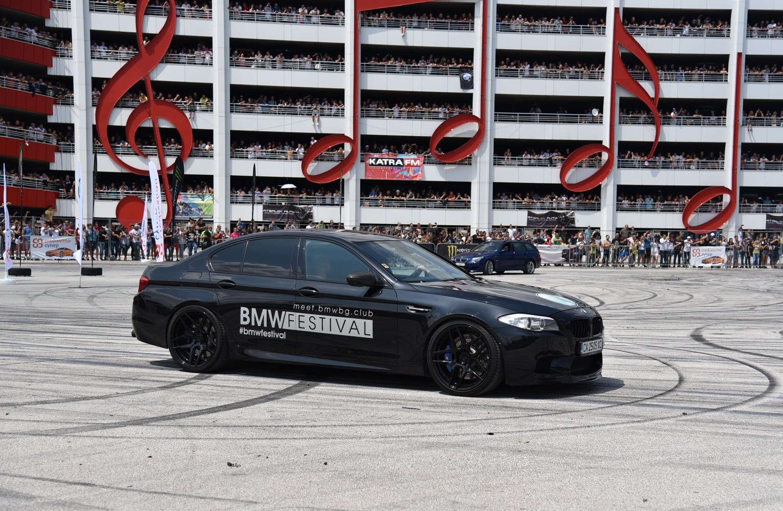 Black sporty sedan with dark wheels and tinted windows on event ground