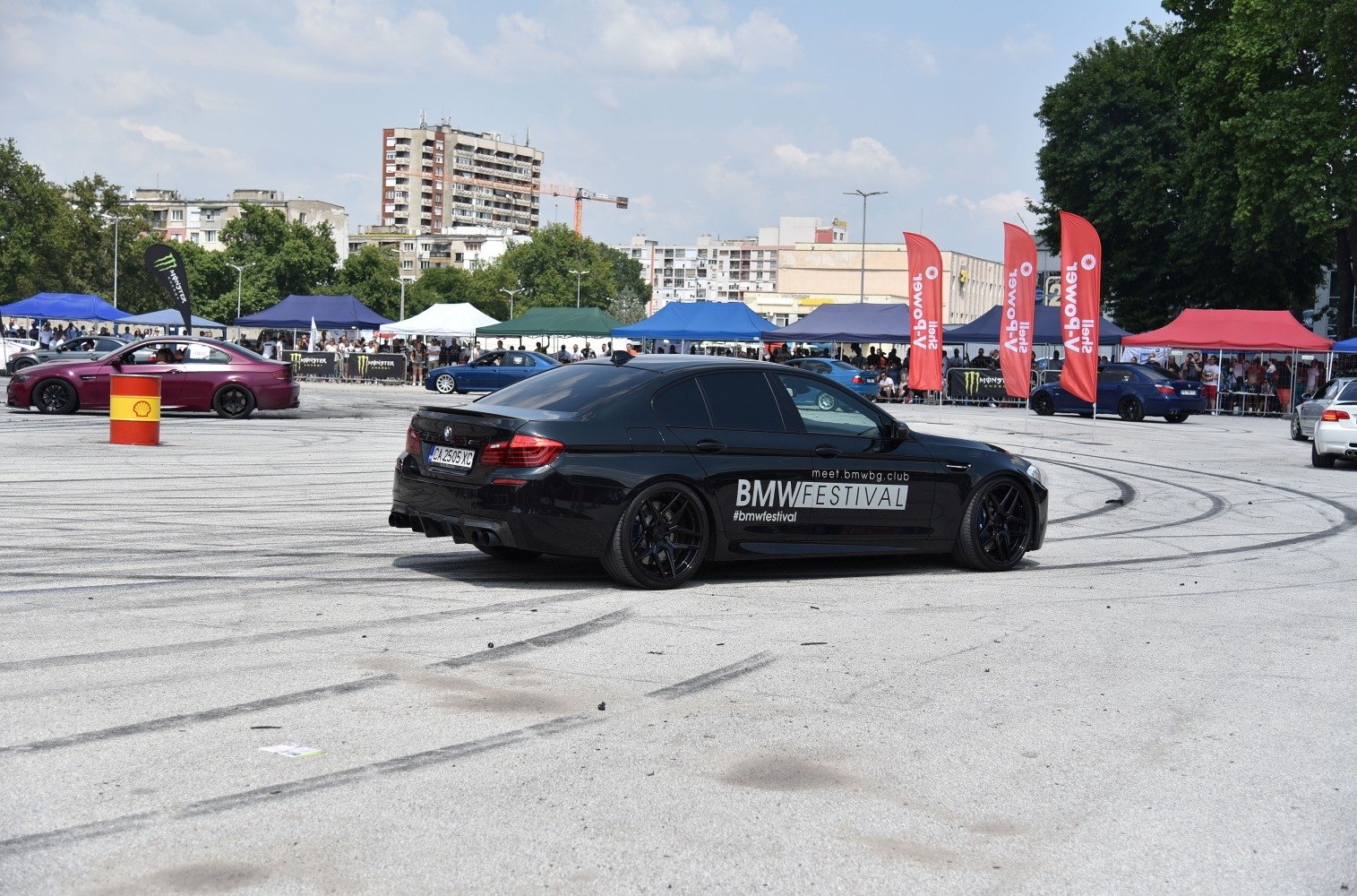 Black sports sedan with aftermarket wheels and tinted windows at a car festival