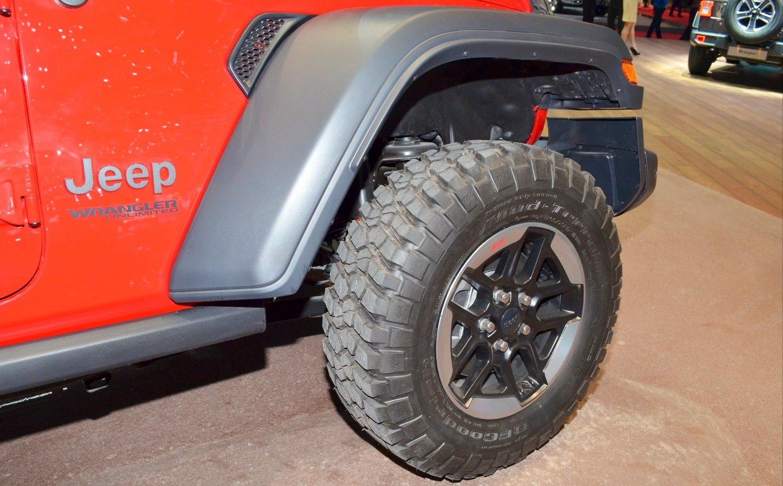 Off-road mud-terrain tire with rugged tread and black alloy wheel on vehicle fender.