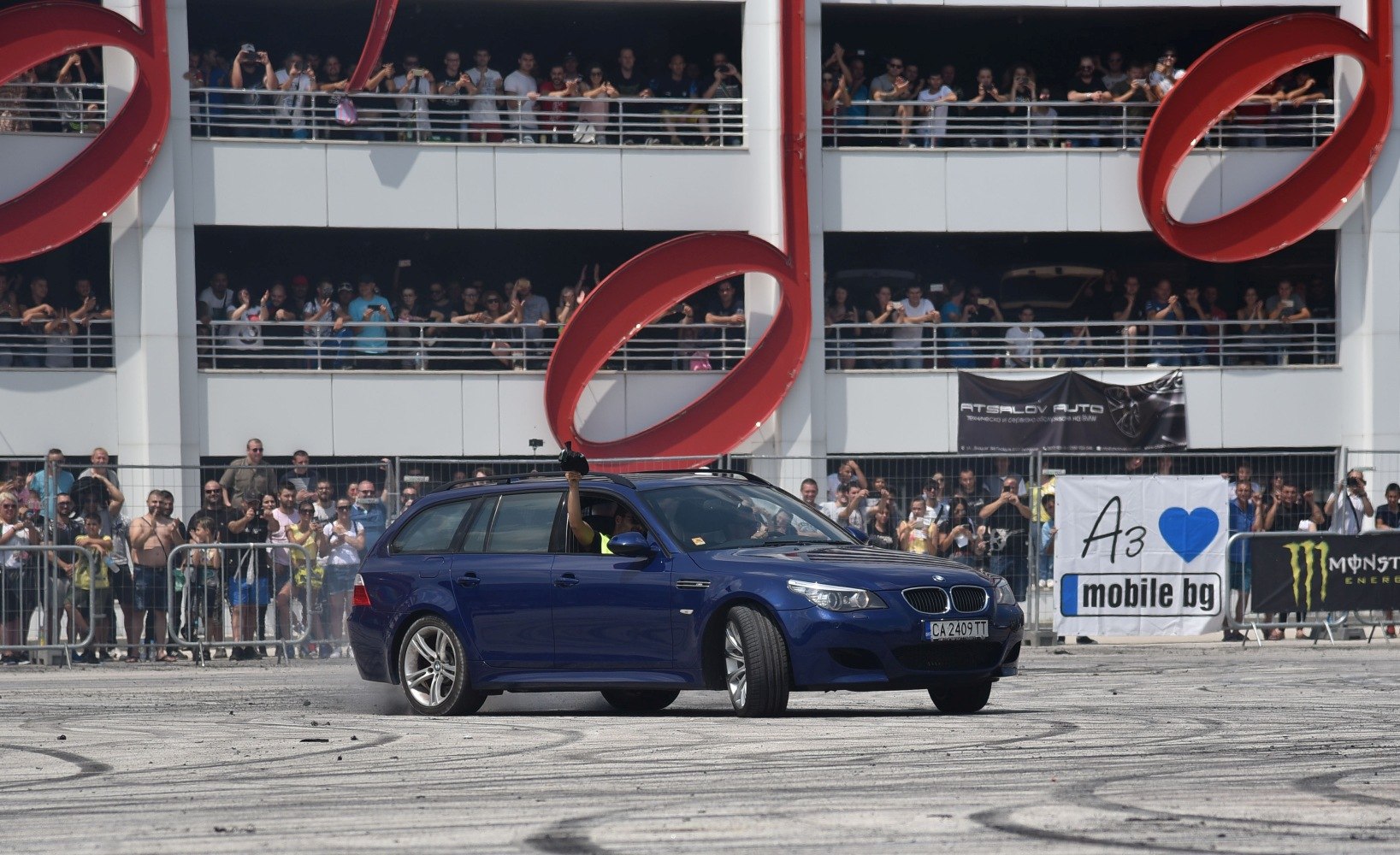 Blue station wagon drifting with tire smoke and crowd