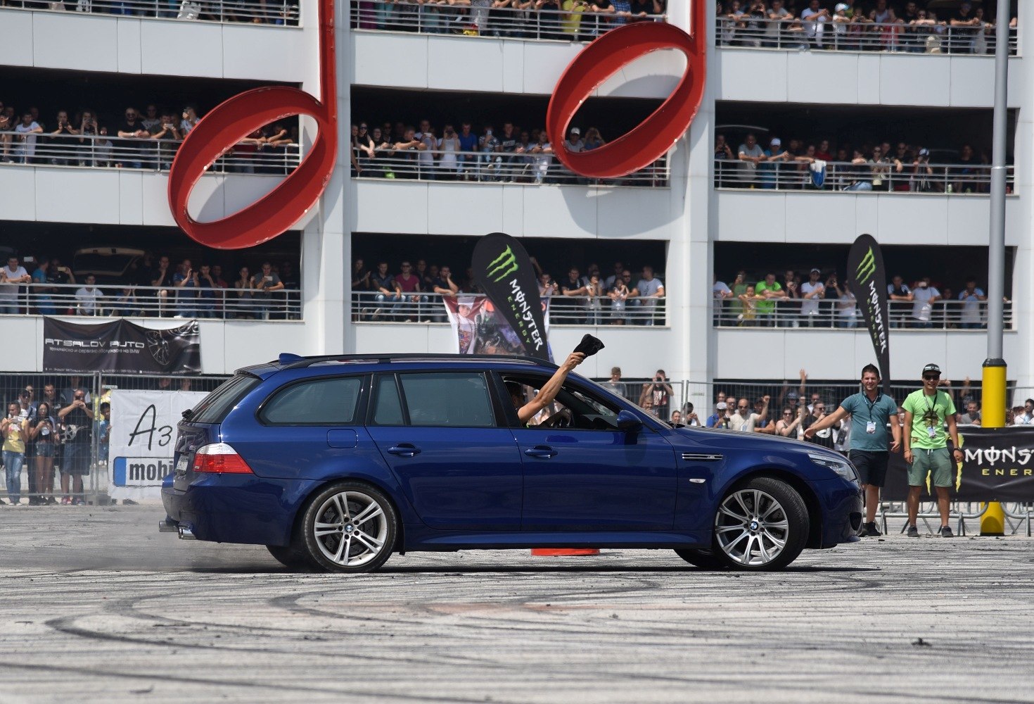 Blue sporty station wagon drifting with tire smoke in front of large crowd