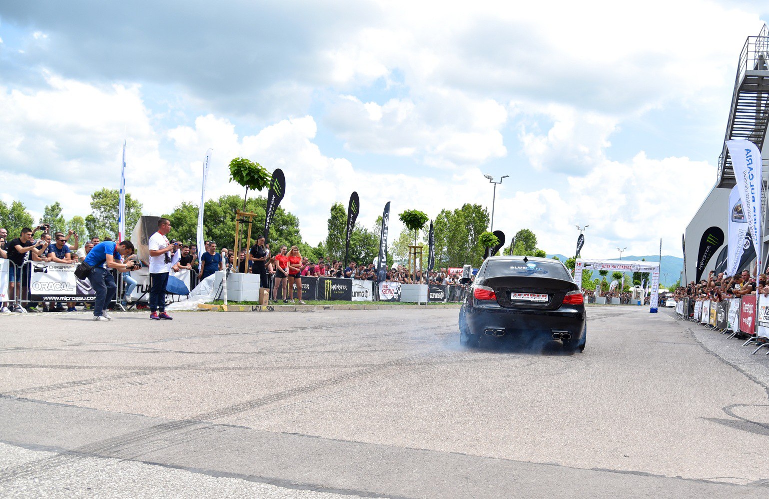 Rear view of a sedan performing a burnout with tire smoke at a crowded event
