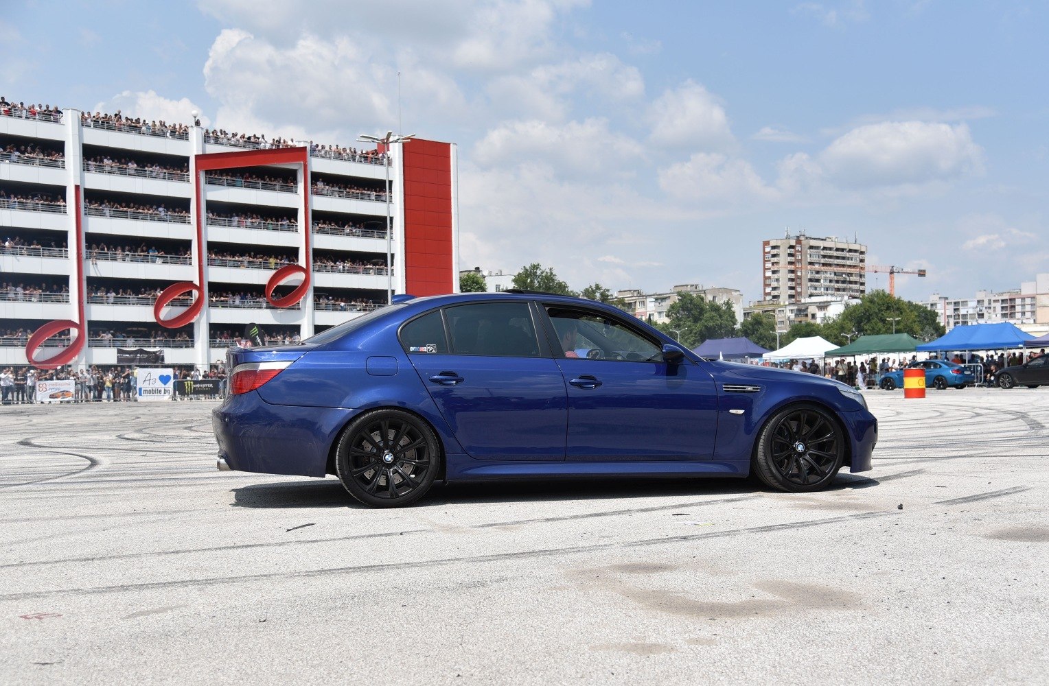 Side profile of blue sports sedan with black wheels on asphalt with tire marks