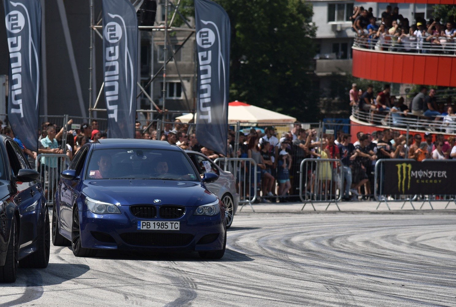 Front view of a dark blue BMW M5 E60 on race track with event crowd