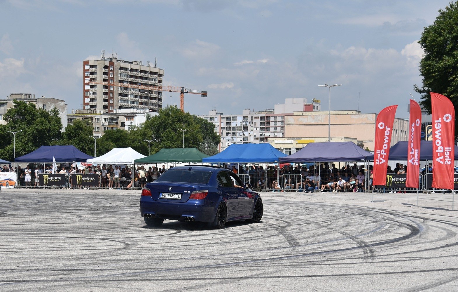 Rear view of a blue sedan drifting with tire marks on asphalt at an event.