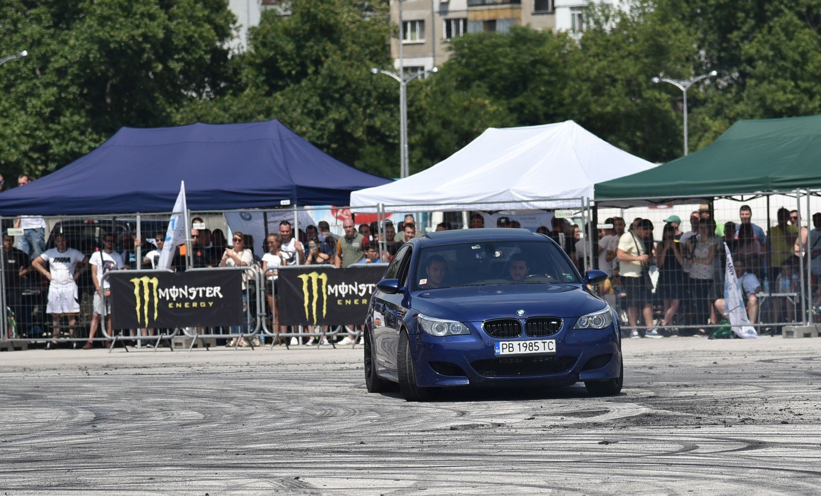 Blue sedan drifting with tire marks and crowd behind