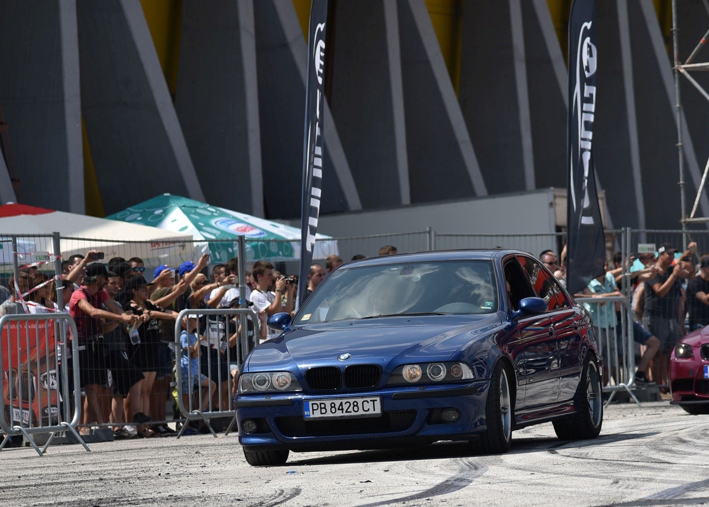 Front view of blue BMW M5 E39 LCI facelift with event crowd