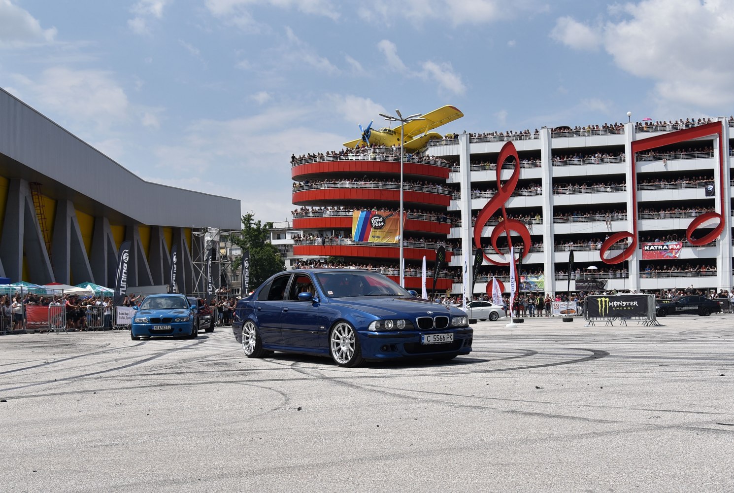 Blue sedan with distinctive headlights and alloy wheels at a busy event.