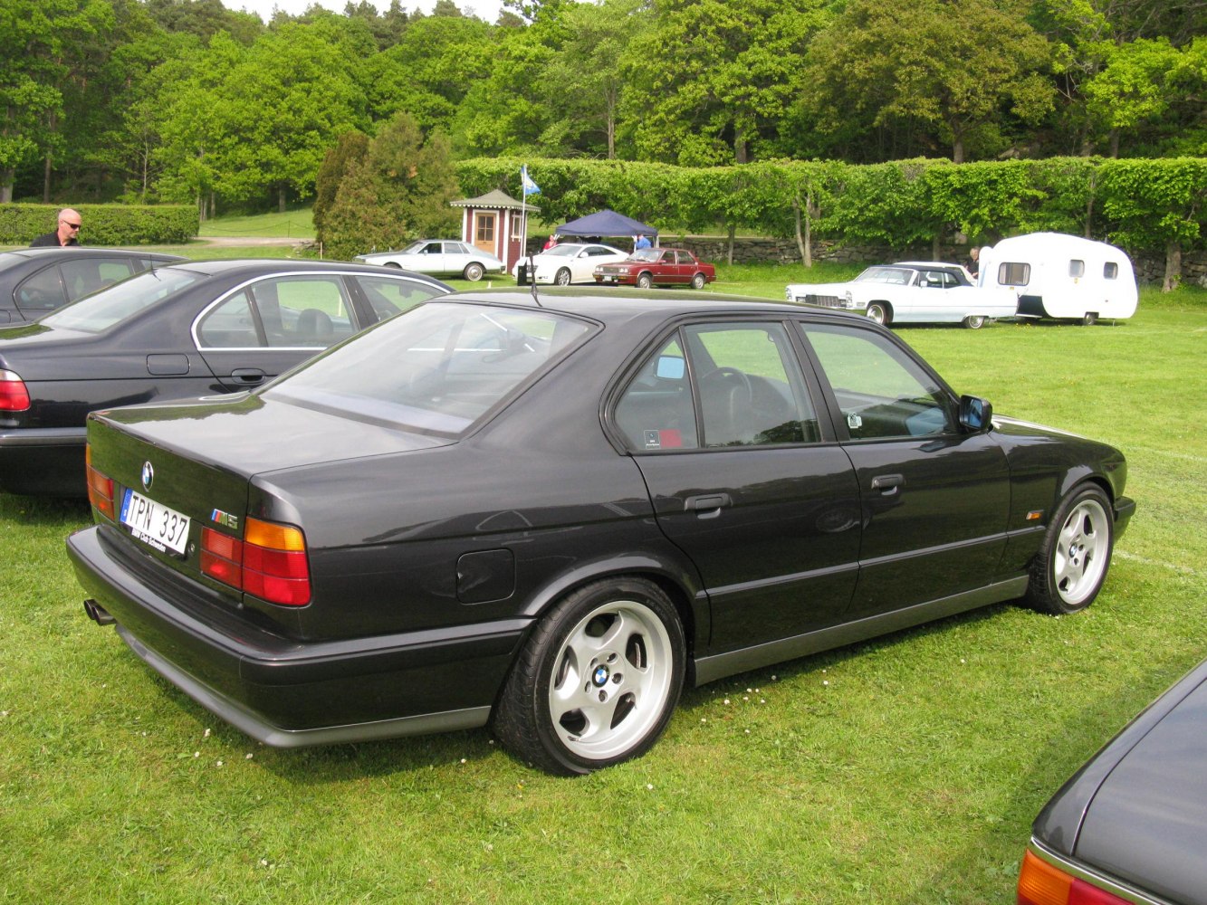 Black BMW E34 M5 rear side view with alloy wheels on grass