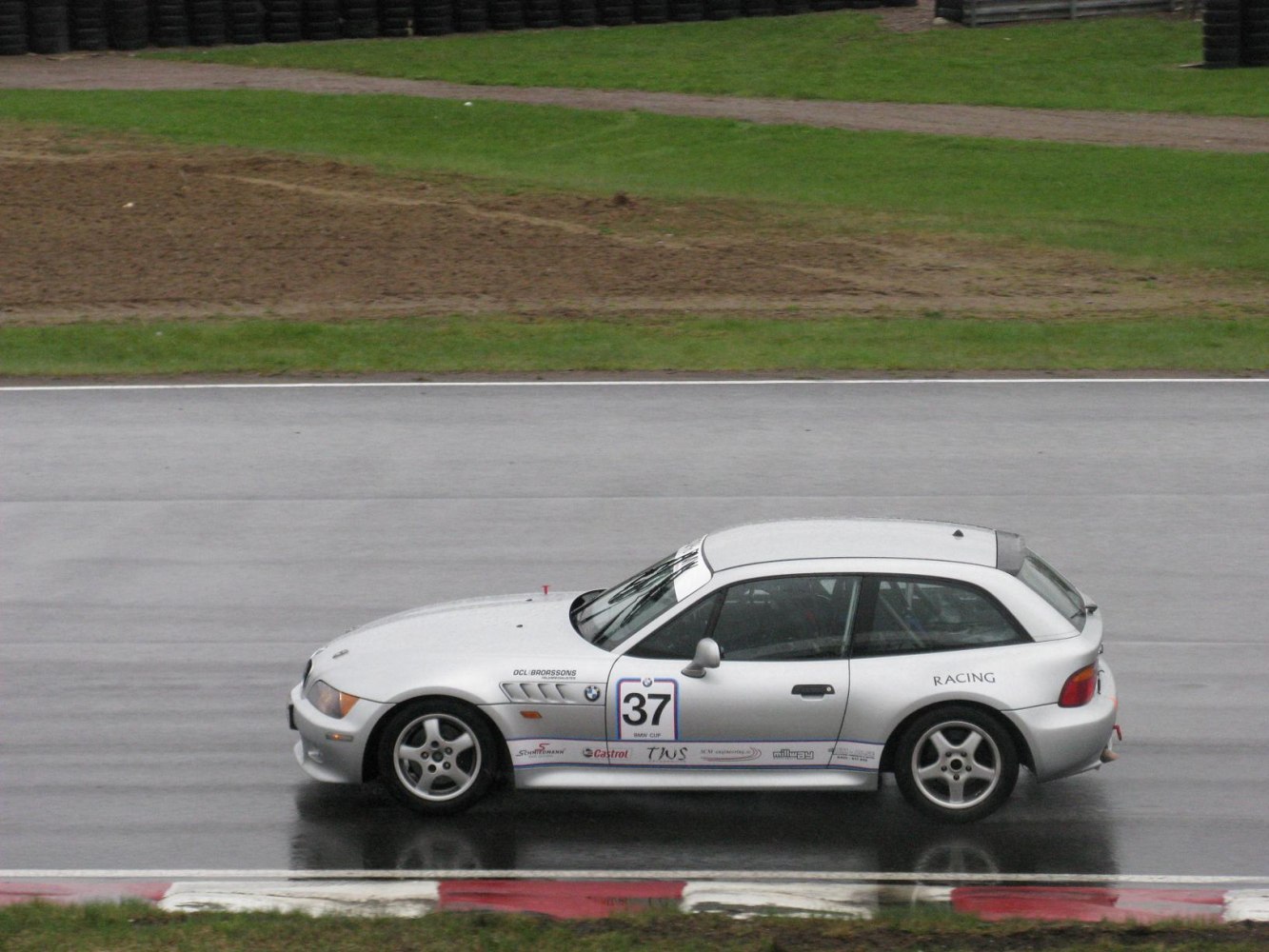 Silver hatchback racing coupe on wet race track
