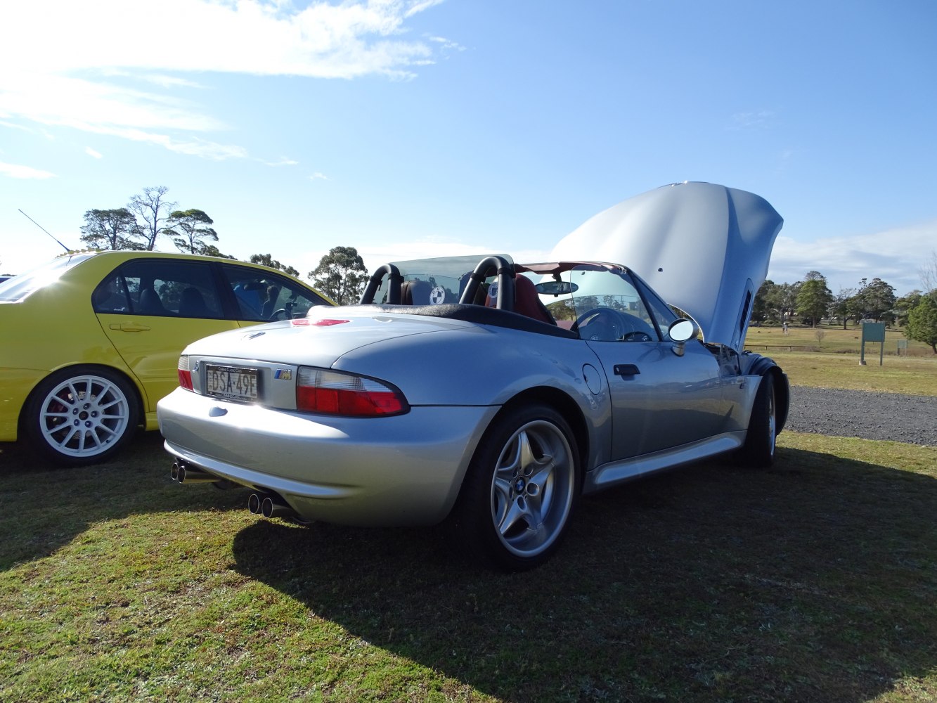 Silver convertible roadster with open hood and dual exhaust tips