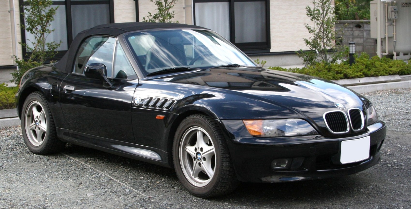 Front side view of a black convertible roadster with distinctive air vents and classic alloy wheels