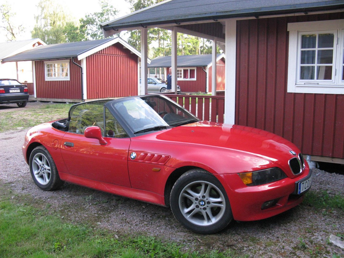 Red convertible sports car with black hardtop parked beside red house
