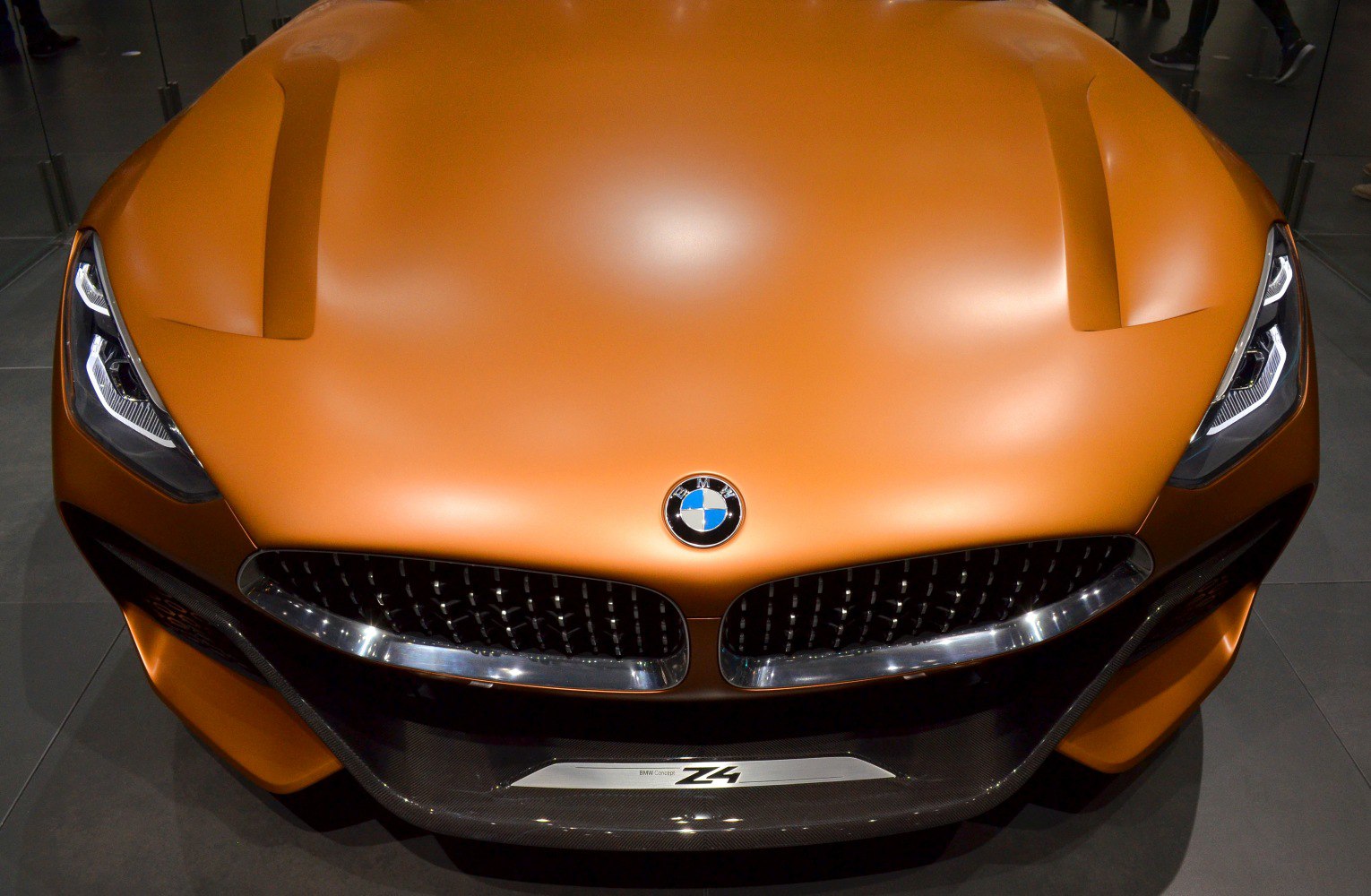 Sleek headlights and kidney grille on matte orange car front.