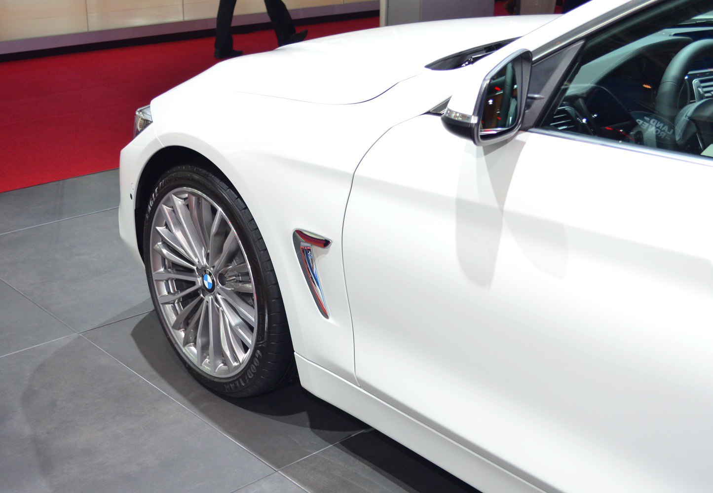 Front wheel, side vent, and side mirror of a white sport coupe