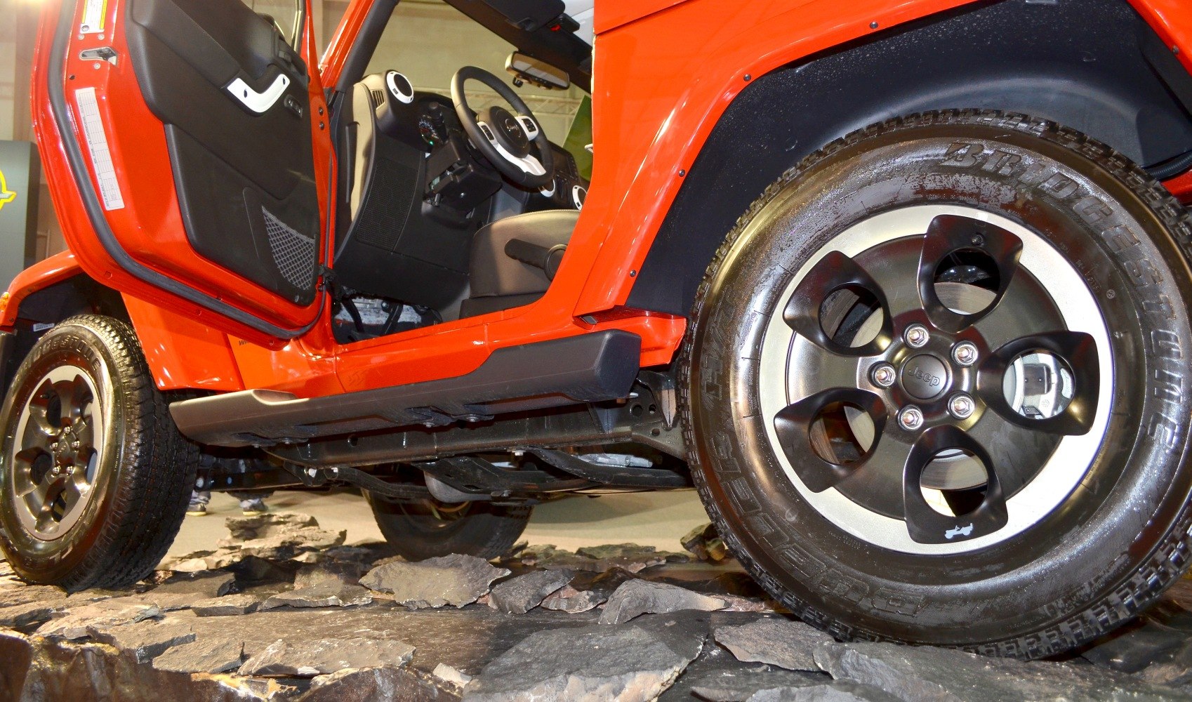 Open driver door with visible interior and detailed alloy wheel on rocky terrain