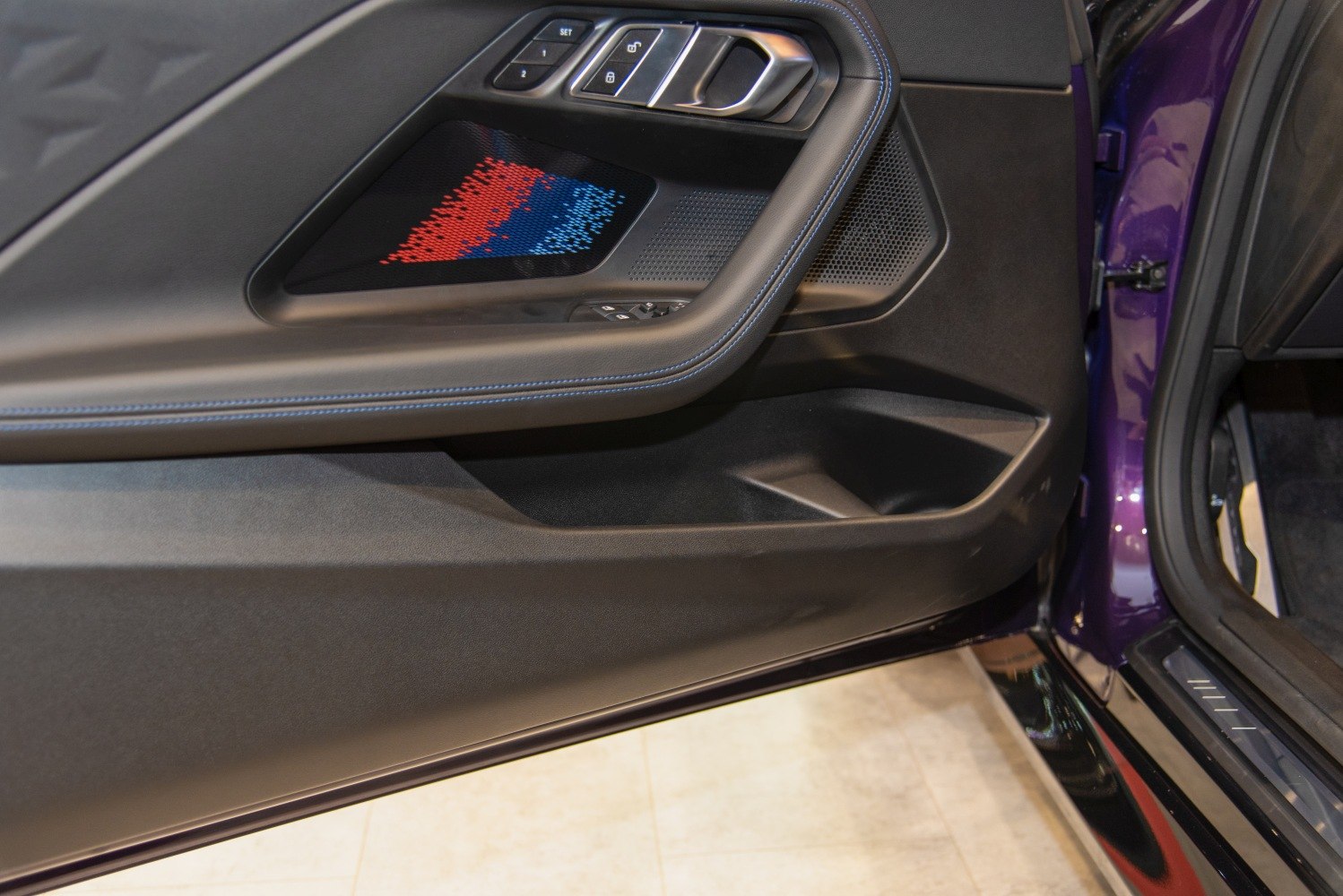 Car door panel with controls, speaker featuring colored design and storage compartment