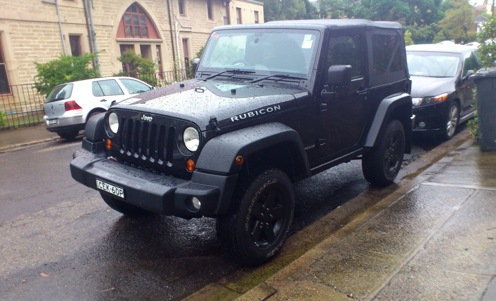 Black SUV with soft top and off-road tires on a wet urban street