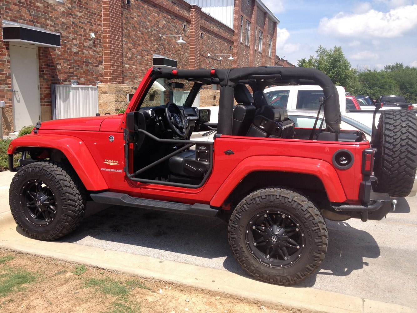 Red vehicle with no doors, black soft top, and off-road tires