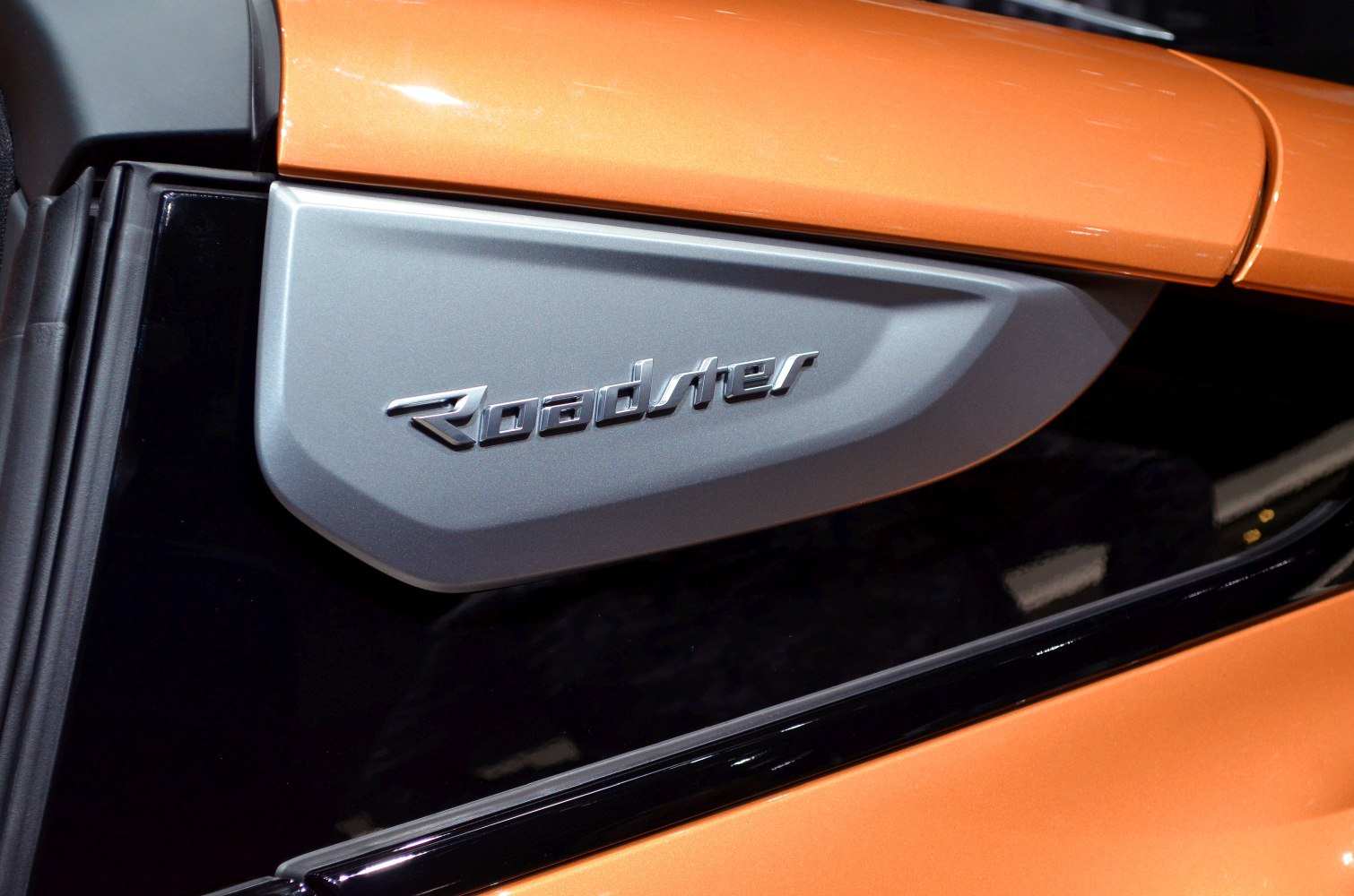 Close-up of Roadster emblem with silver badge on orange body panel.