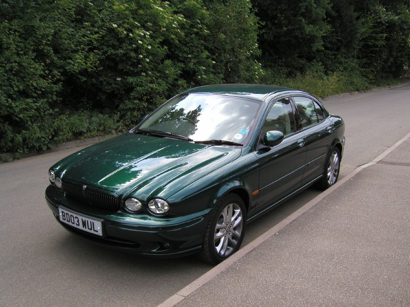 Green sedan with dual round headlamps and alloy wheels.
