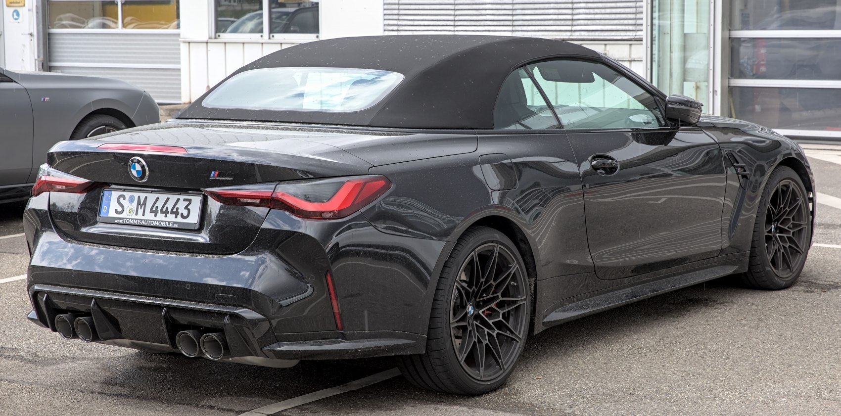 Rear view of a black convertible with soft top and quad exhaust pipes.