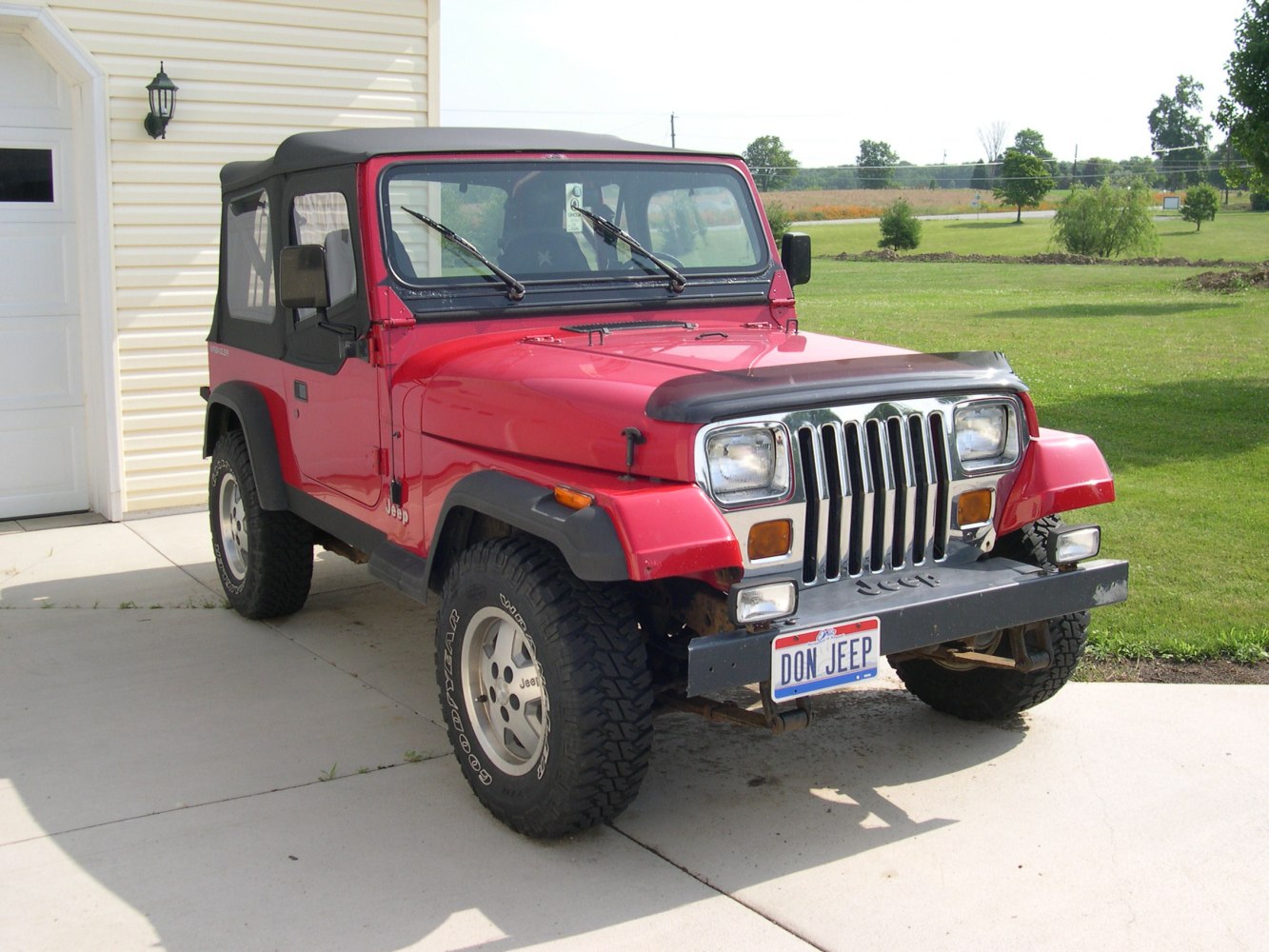 Red Jeep with soft top, front grille, and off-road tires
