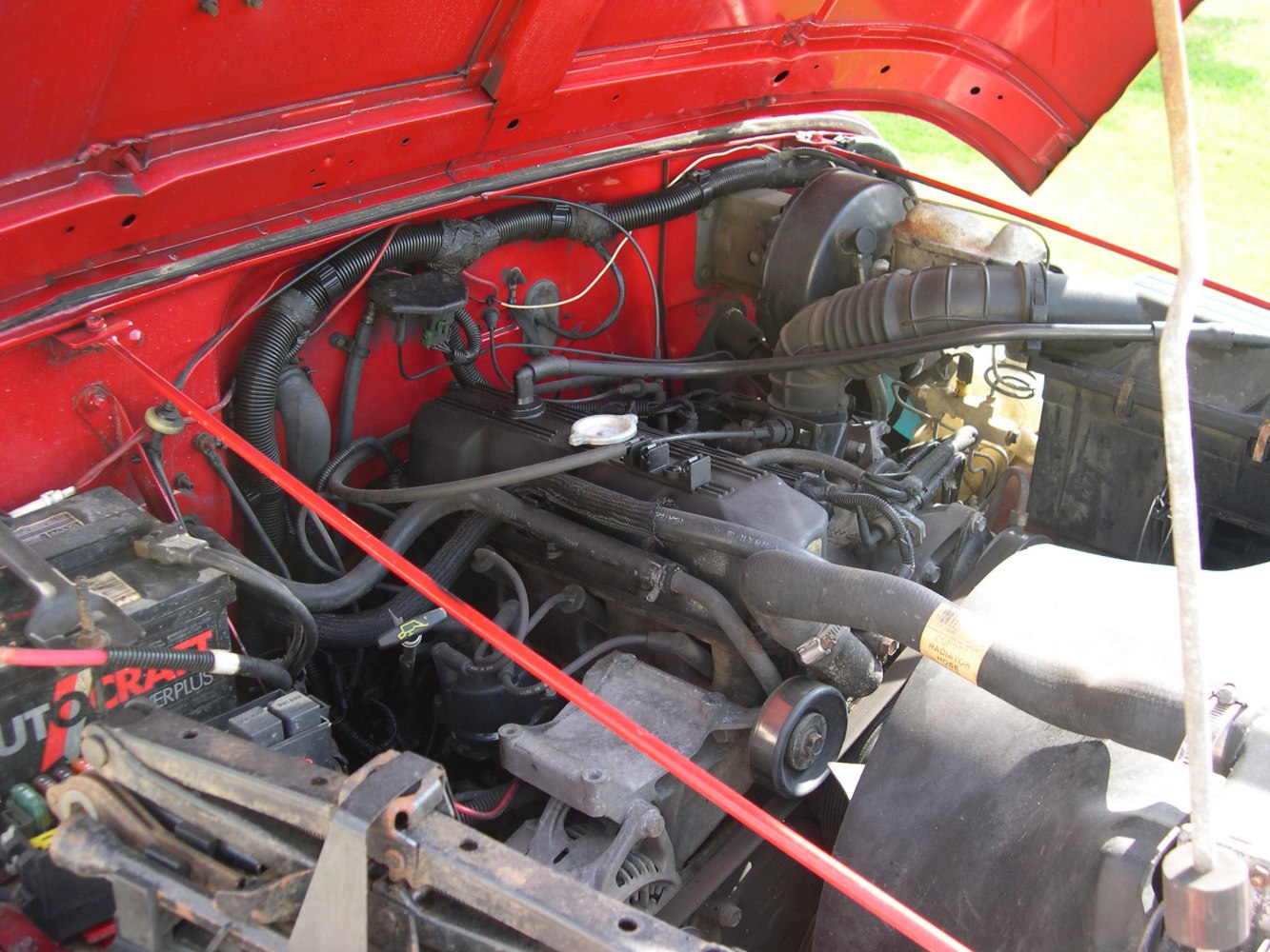 Close-up of engine bay showing wiring, battery, radiator hose, and air intake tubing