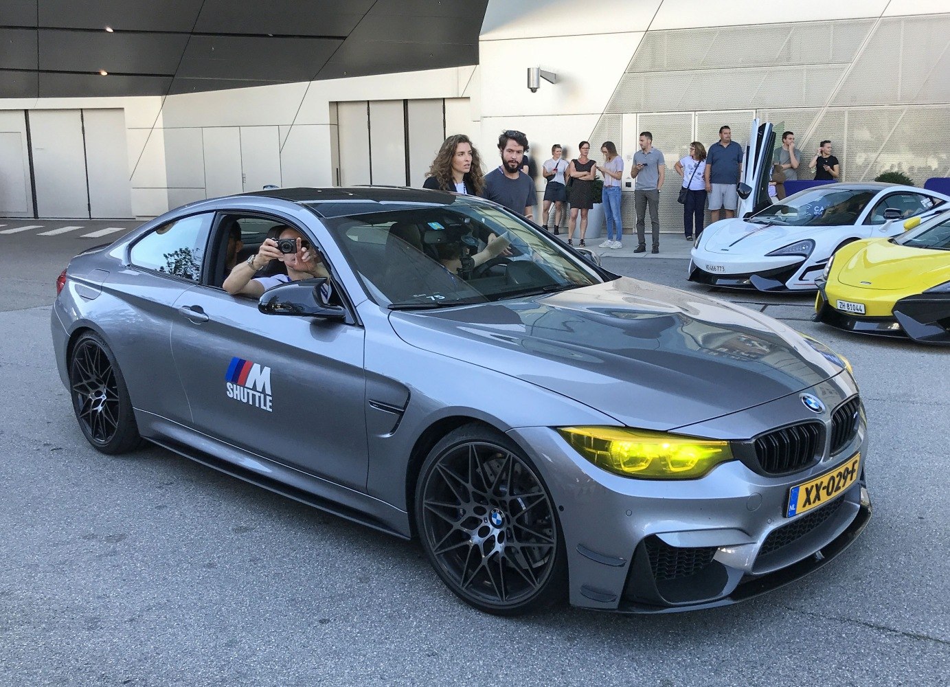 Grey coupe with yellow headlights, M Shuttle logo, and black multi-spoke wheels