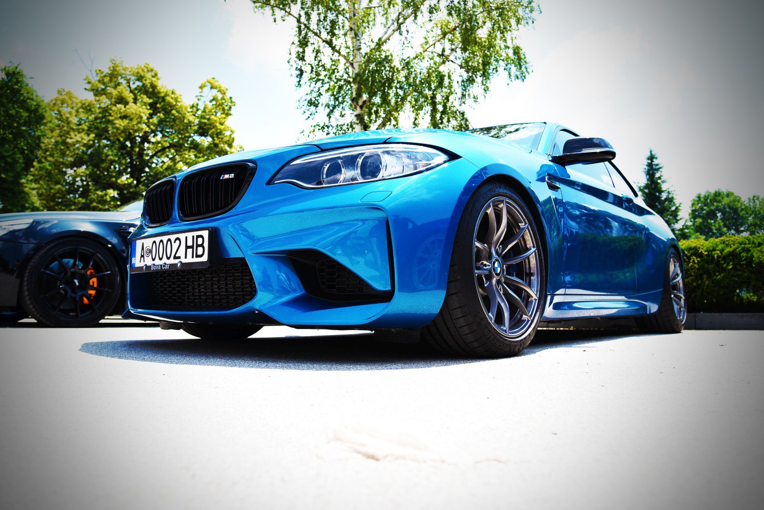 Close-up of front headlight, grille, and sporty wheel of blue aggressive performance coupe