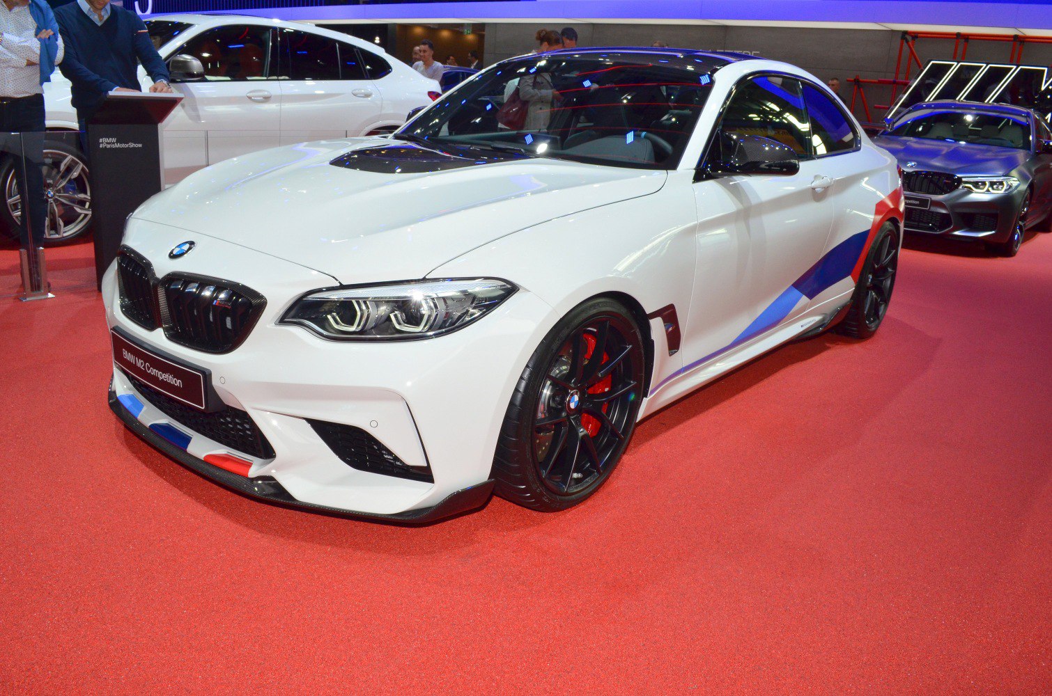 White coupe with carbon fiber hood, racing stripes, black multi-spoke wheels, red brake calipers
