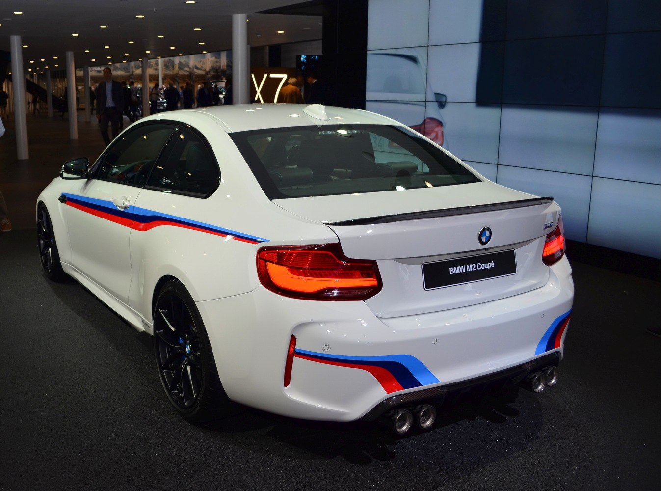 Rear view of a white sporty coupe with M stripes and quad exhaust tips