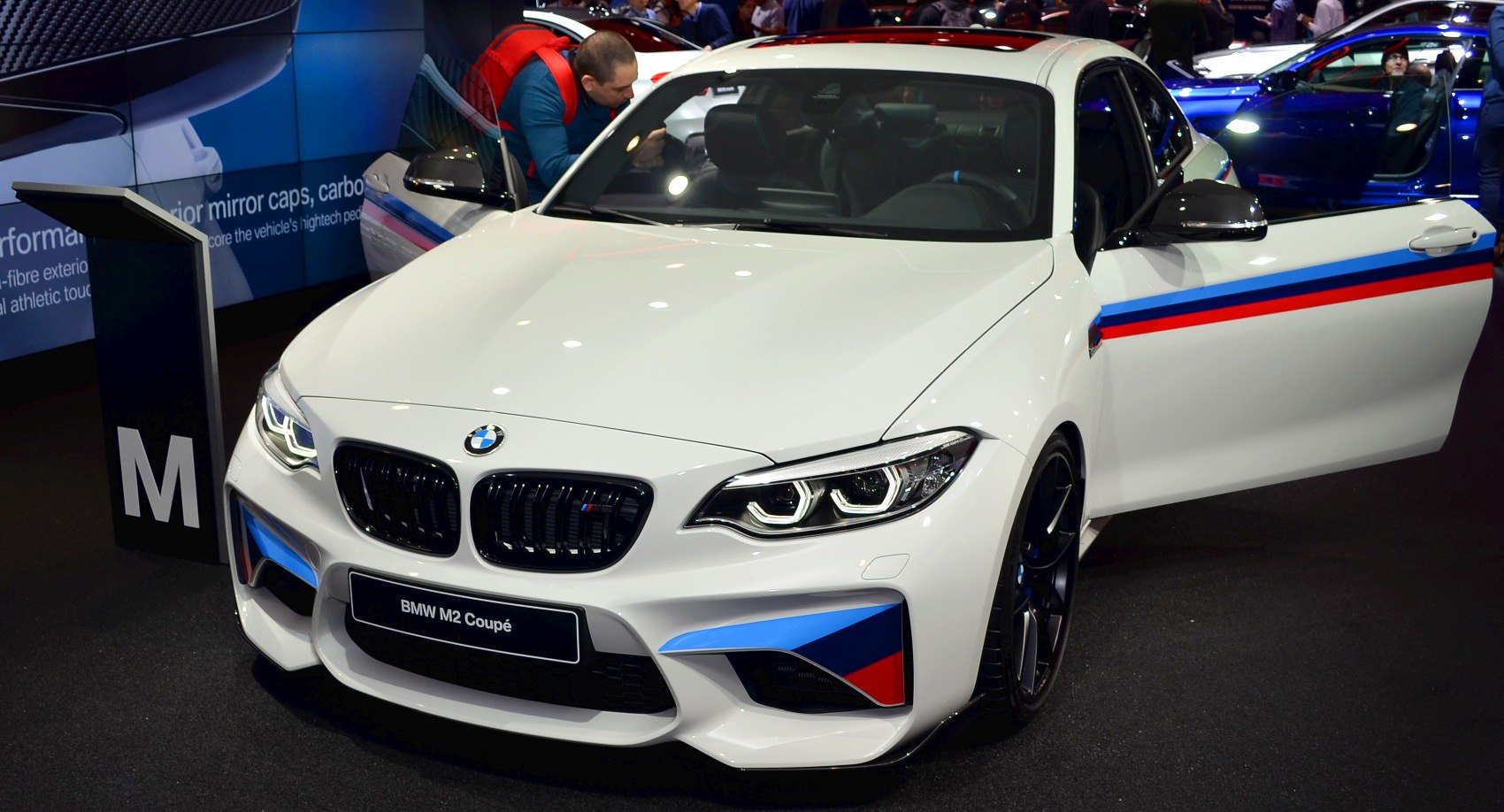Front view of a sporty coupe with distinctive M stripes and LED headlights, door open.